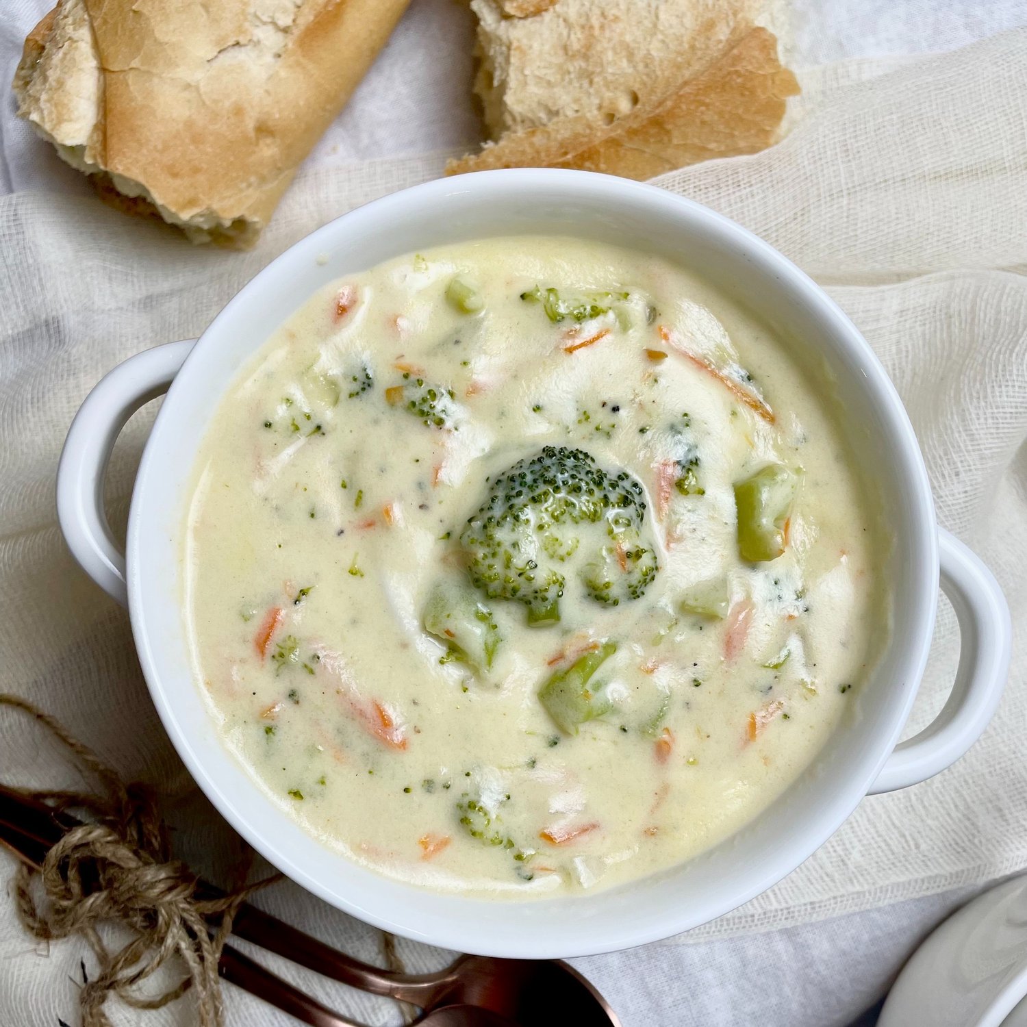 broccoli cheddar soup in a white serving bowl with crusty french bread on the side