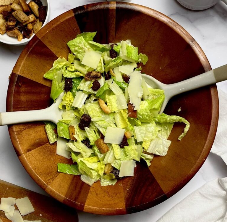 caesar salad in a wooden serving bowl with serving spoons