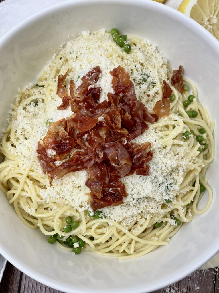 prosciutto lemon pasta in a white serving bowl on a picnic table. close up view of the crispy prosciutto on top.