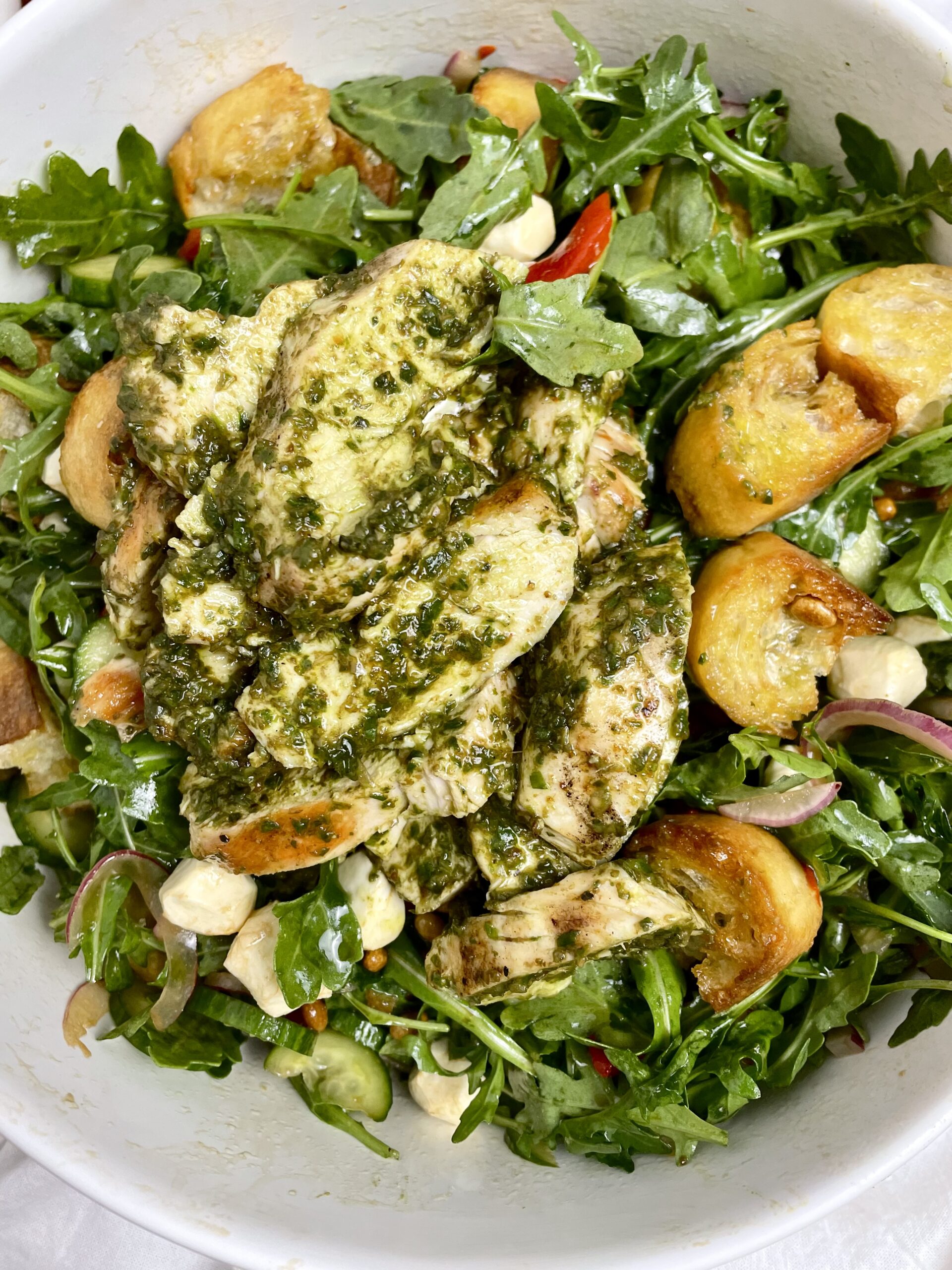arugula salad with mozzarella cheese in a white salad bowl with pesto chicken on top