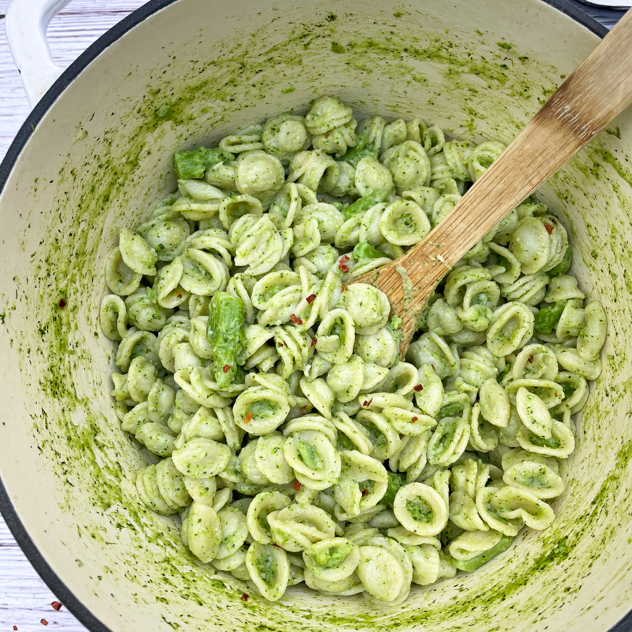 close up image of orecchiette con broccoli in a white enameled cast iron pot with a bamboo serving spoon.