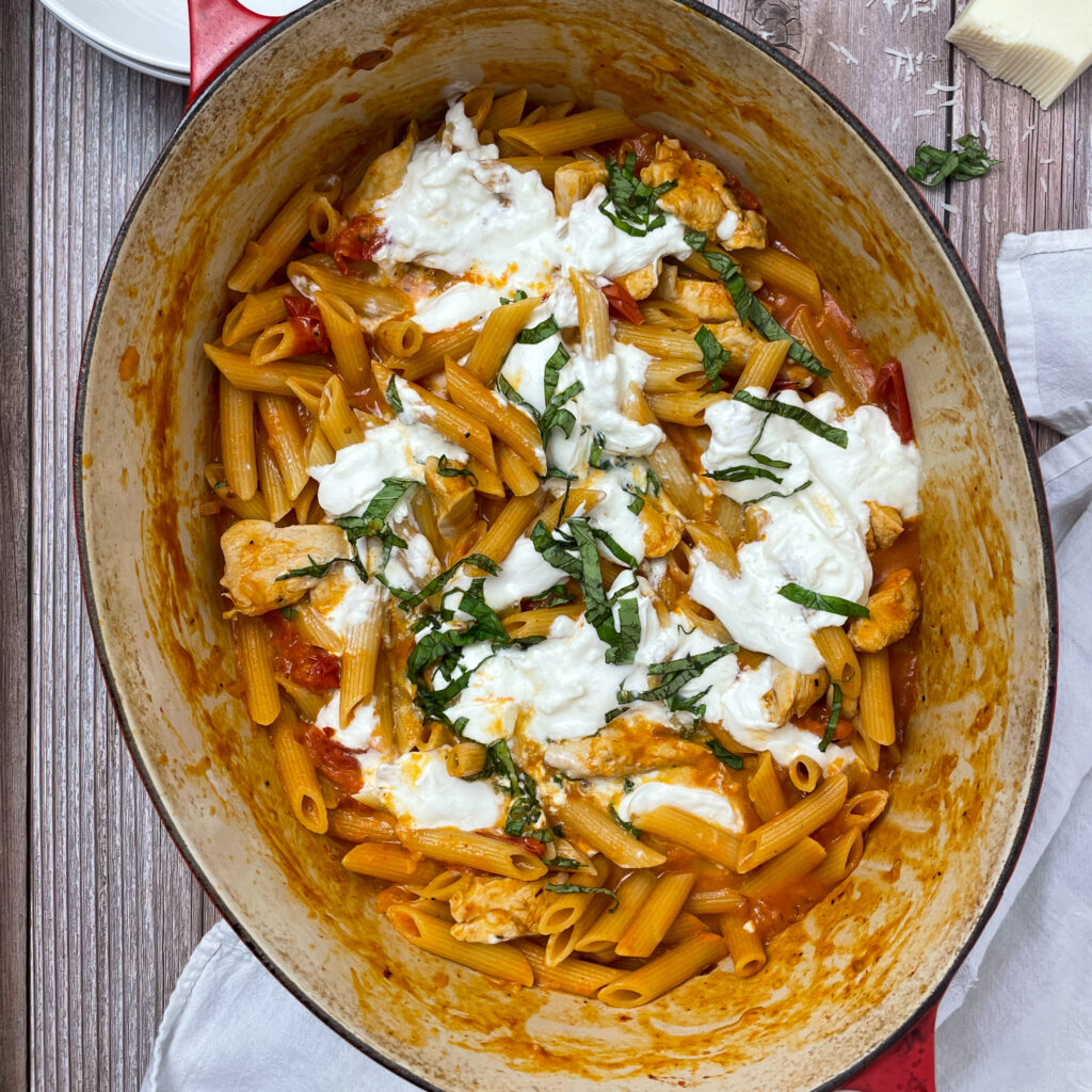 margherita chicken pasta in a enameled cast iron dutch oven pot with burrata cheese torn on top with chopped basil