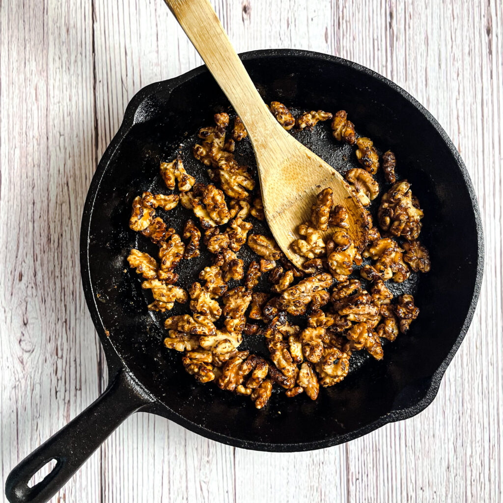 maple toasted walnuts in a medium cast iron skillet with a bamboo serving spoon on a white picnic table.