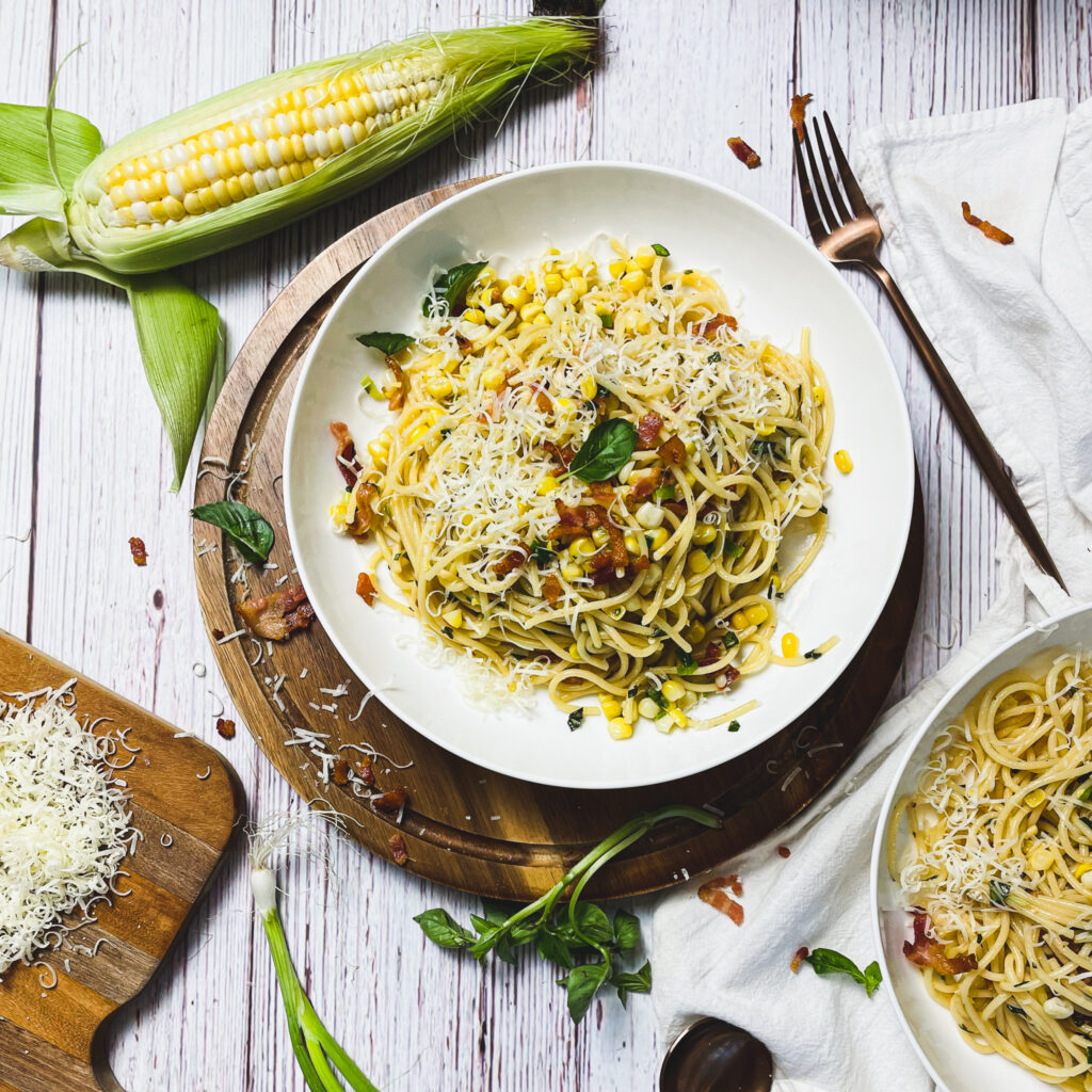 Bacon and sweet corn pasta in a white pasta bowl on a wooden serving platter, placed on a white picnic table