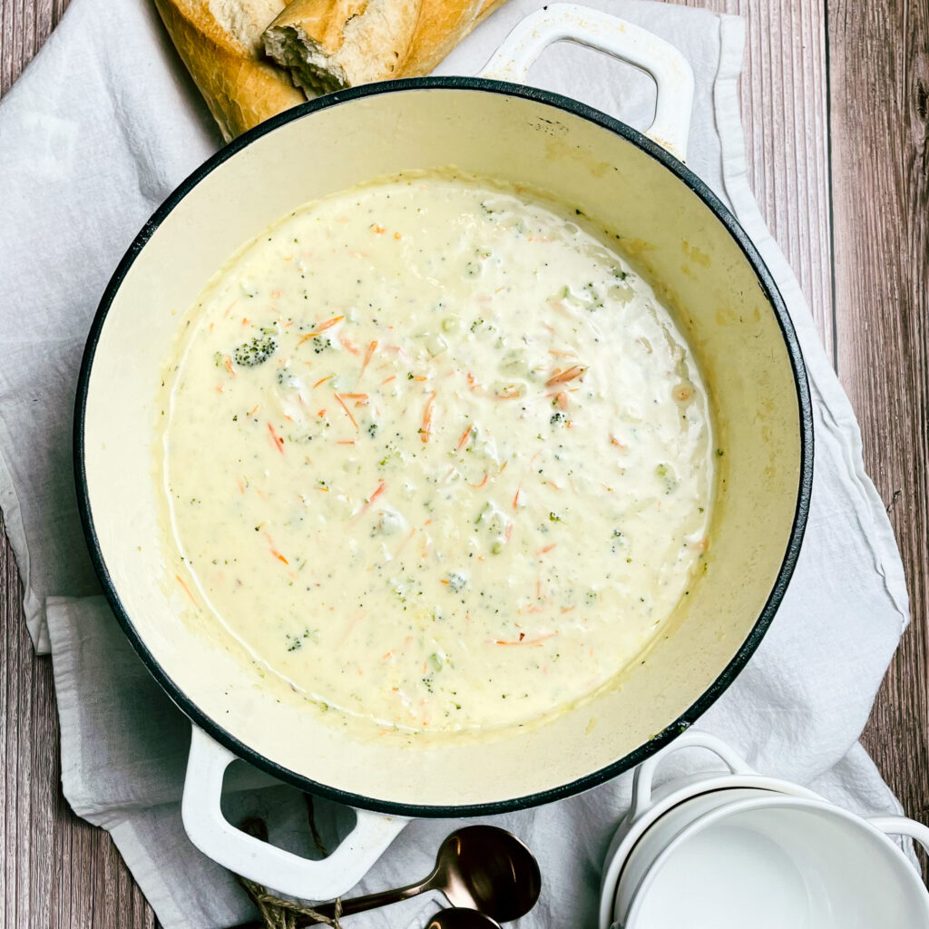 30 minute cheddar broccoli soup in a white enameled dutch oven on a white table cloth with a broken loaf of French bread