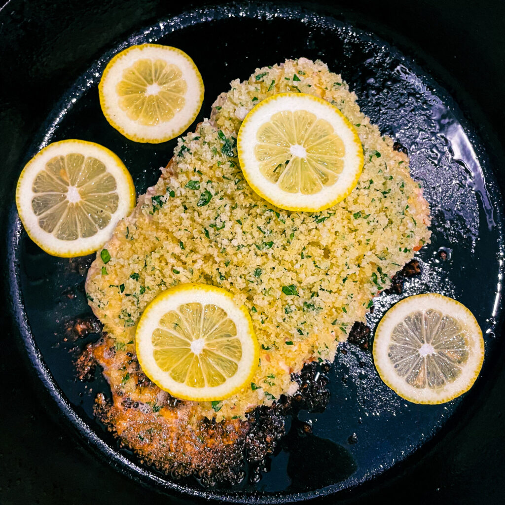 maple dijon panko crusted salmon in a cast iron skillet topped with slices of fresh lemon