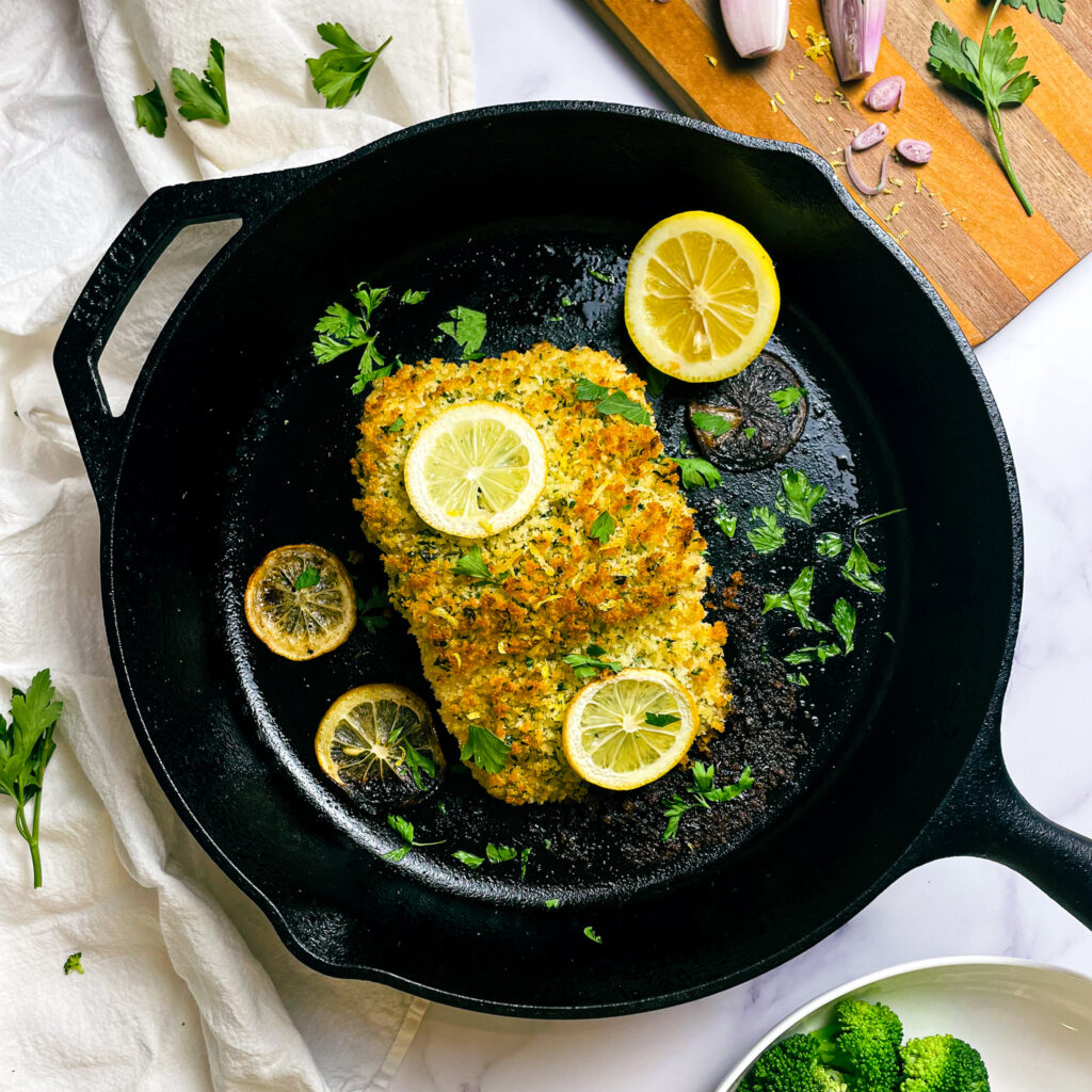 cooked maple dijon panko crusted salmon in a cast iron skillet on a kitchen table for serving, with sliced lemon and fresh parsley in the pan.