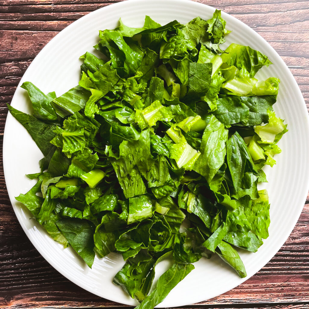 white salad bowl on a brown picnic table with sliced lettuce