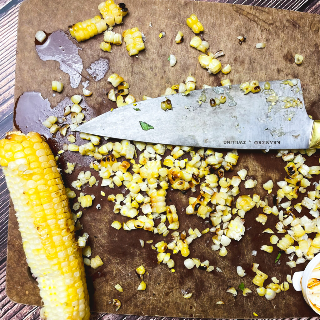 charred corn on the cob on a cutting board with the kernels sliced off