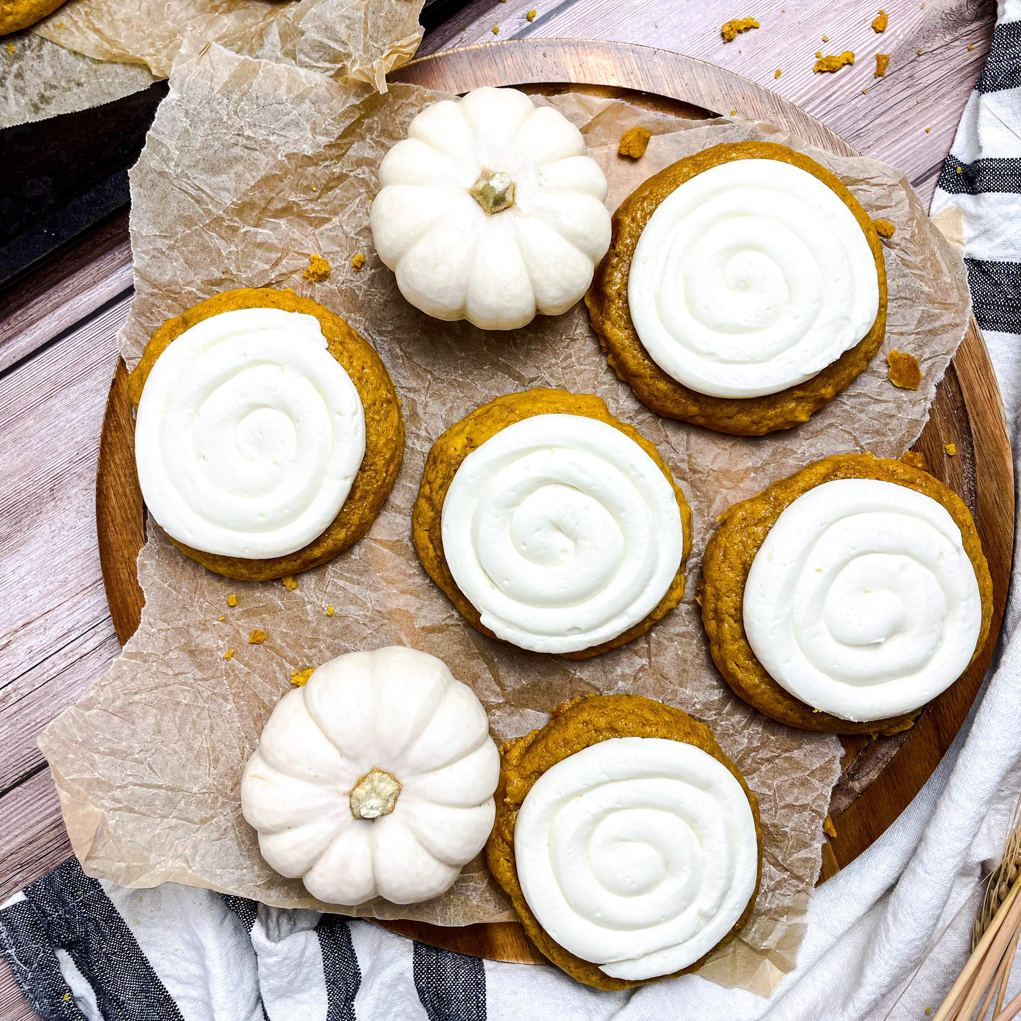 crumbl pumpkin cookies on a wooden plate on parchment paper with a few white mini pumpkins scattered