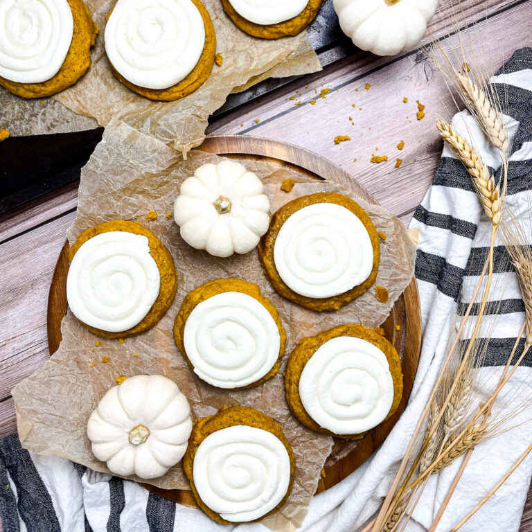 crumbl pumpkin cookies on a wooden plate on parchment paper with a few white mini pumpkins scattered