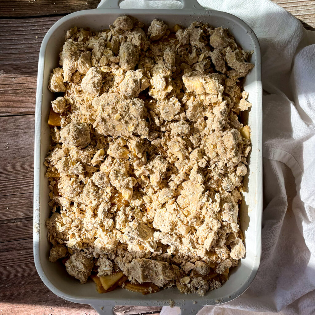 the apple crisp assembled with the crisp topping before baking in a white casserole dish on a wooden table
