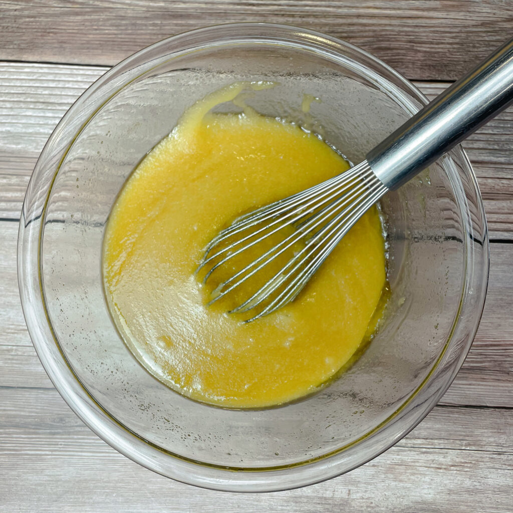 Melted butter, sugar, vanilla extract and eggs in glass mixing bowl mixed together with a metal whisk.