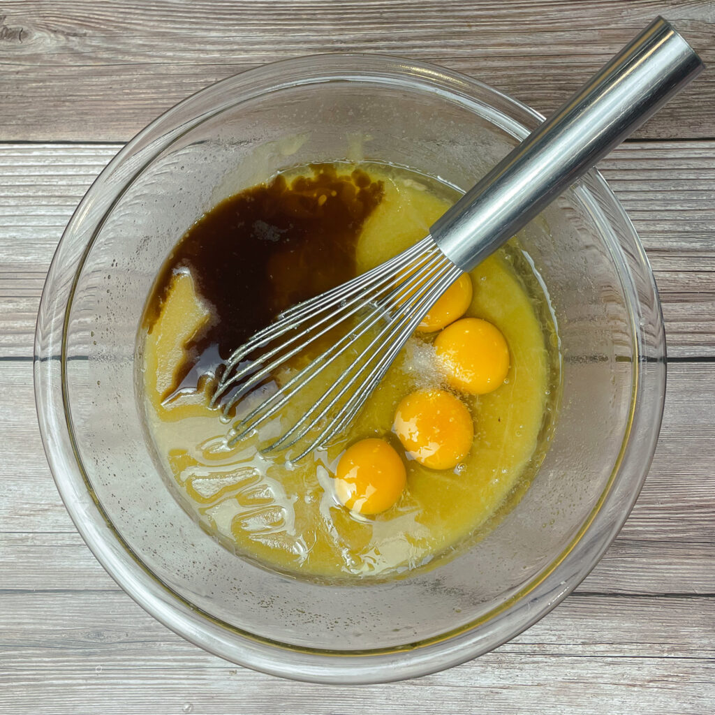 Melted butter, sugar, vanilla extract and eggs in a glass mixing bowl to be mixed together.