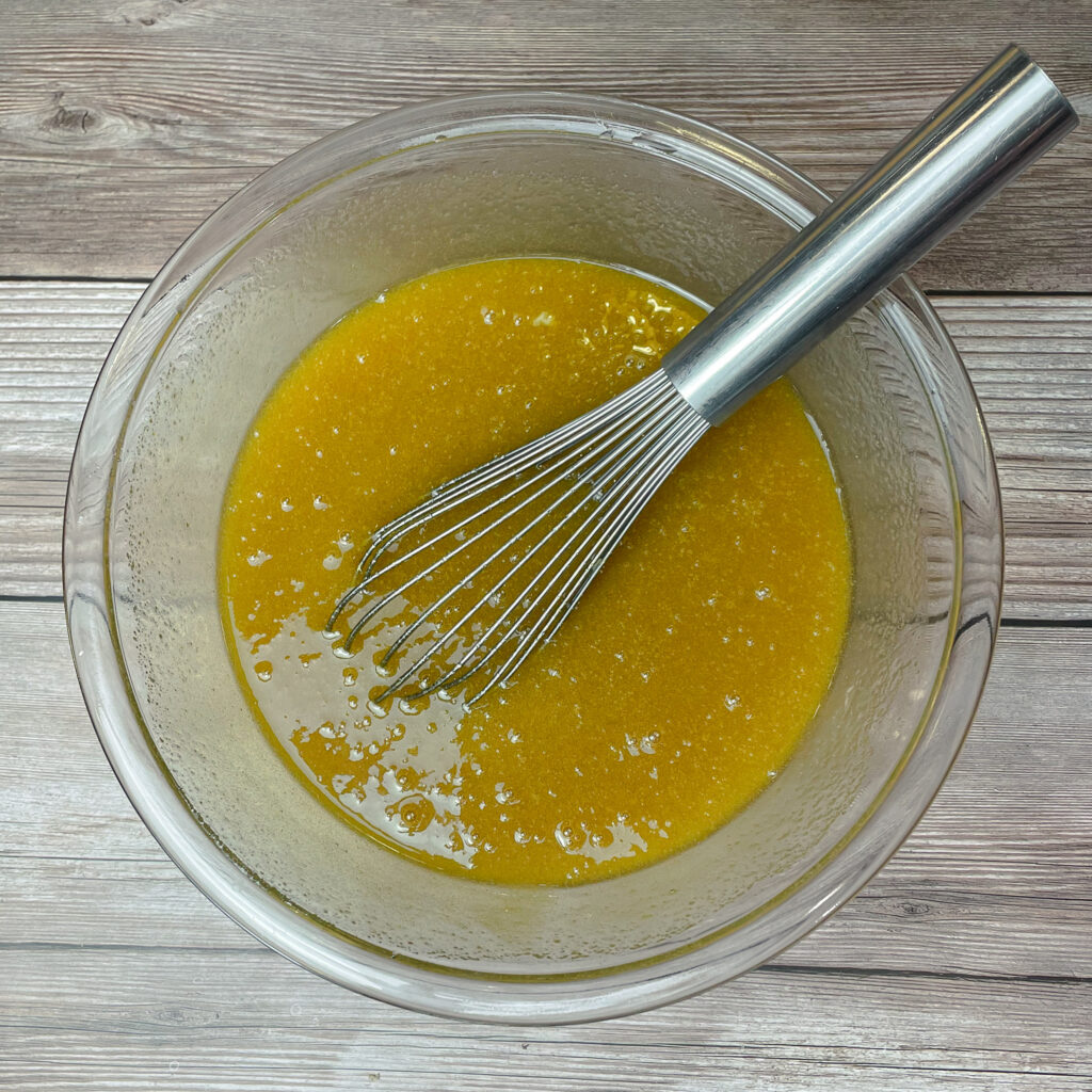 Melted butter and sugars mixed together in a glass mixing brown for the brownie batter.