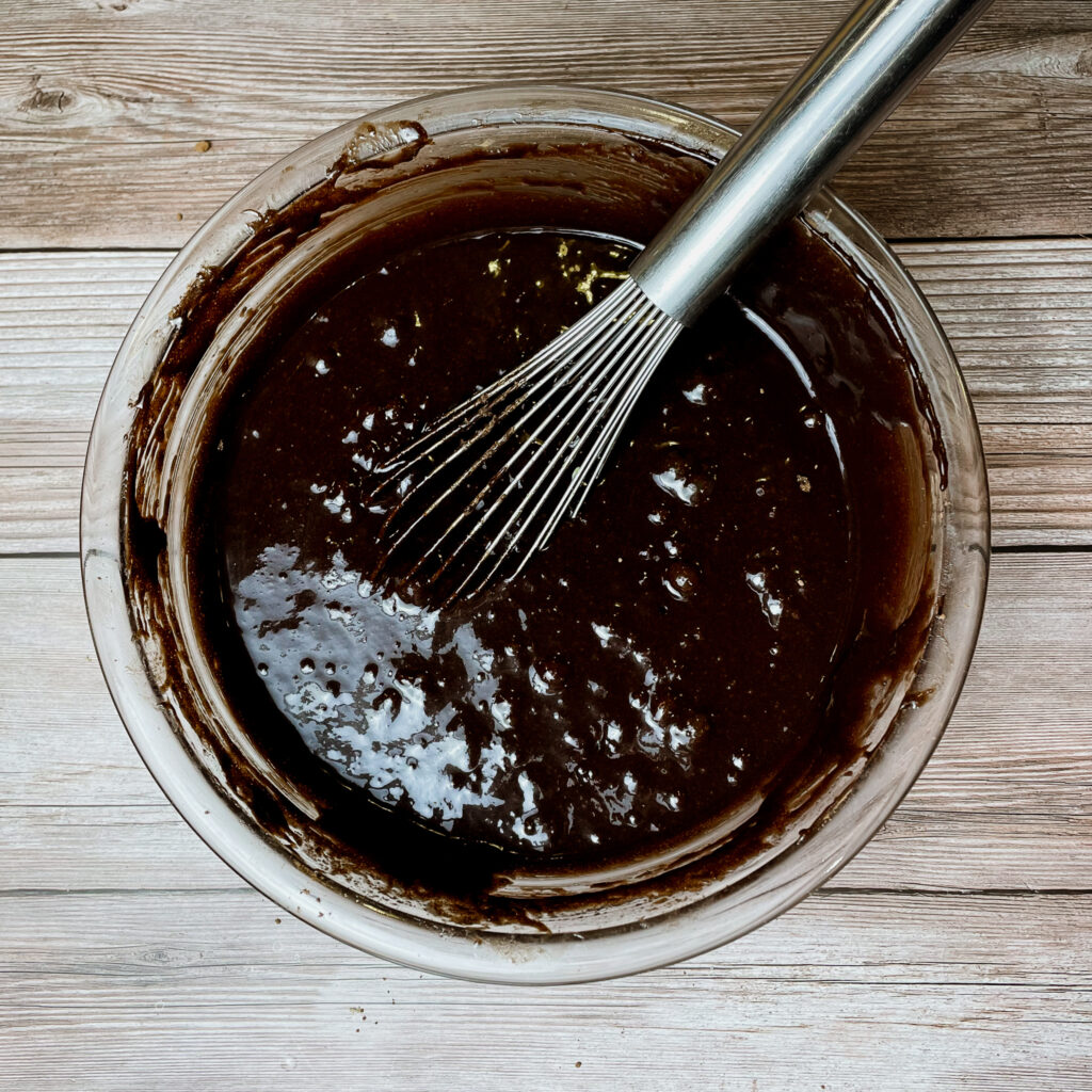 brownie batter ingredients in a glass mixing bowl with the cocoa powder just mixed in with a metal whisk.