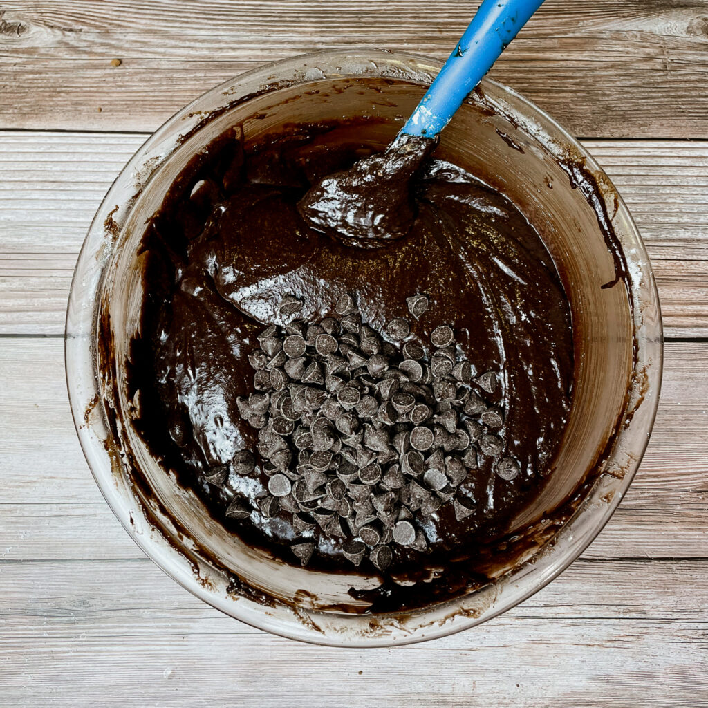 brownie batter in a mixing bowl with chocolate chips on top to be mixed in