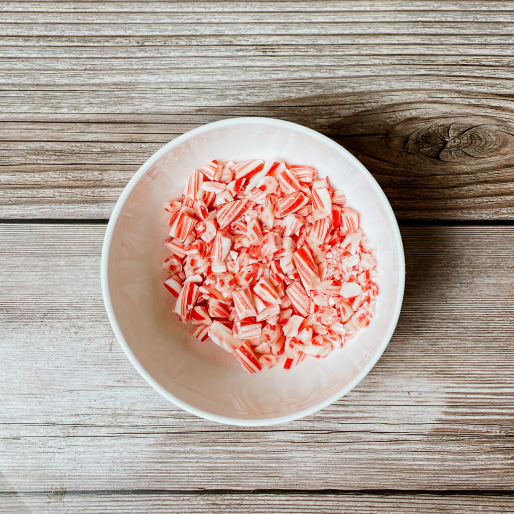 Crushed candy canes in a small white bowl on wooden countertop.