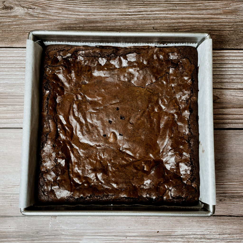 Baked brownies in an 8x8 metal pan set on a wooden countertop.
