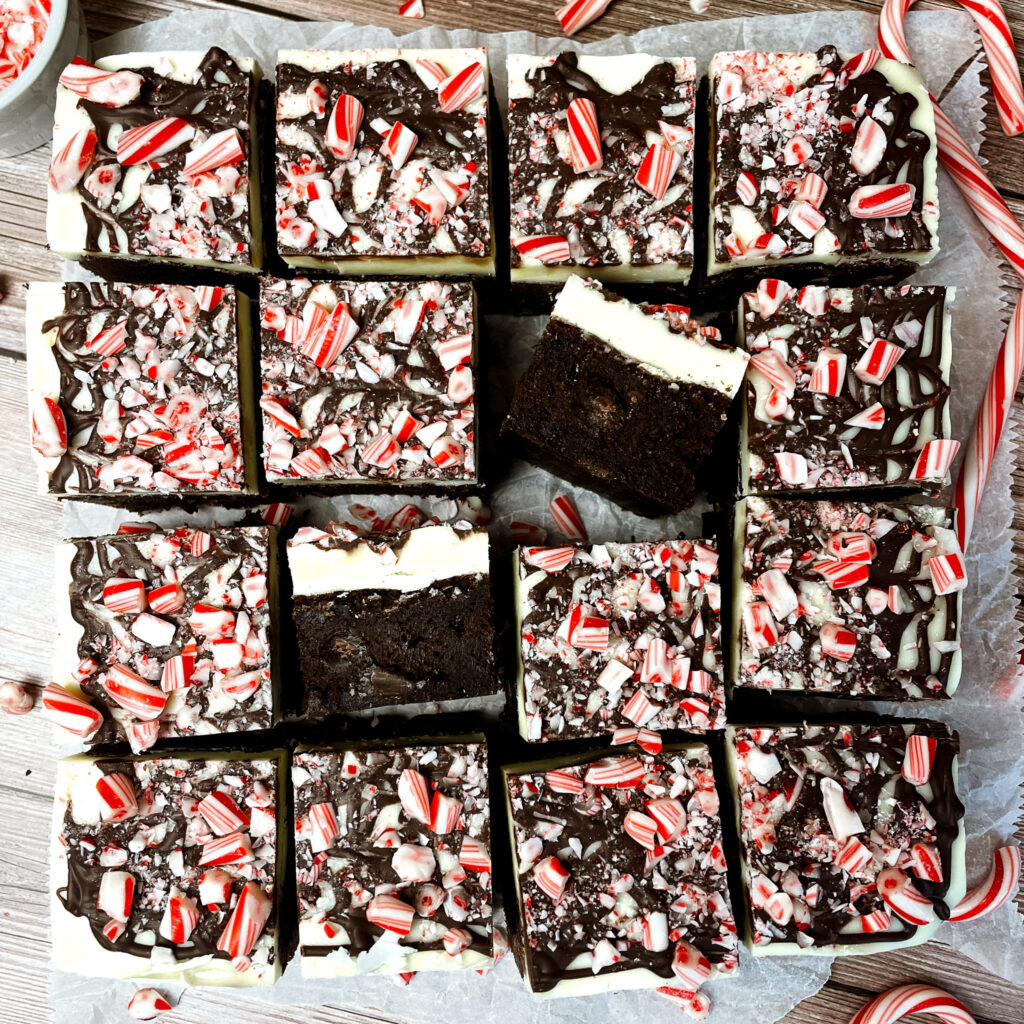 Peppermint bark brownies cut into small squares with candy canes laying around the counter beside them.