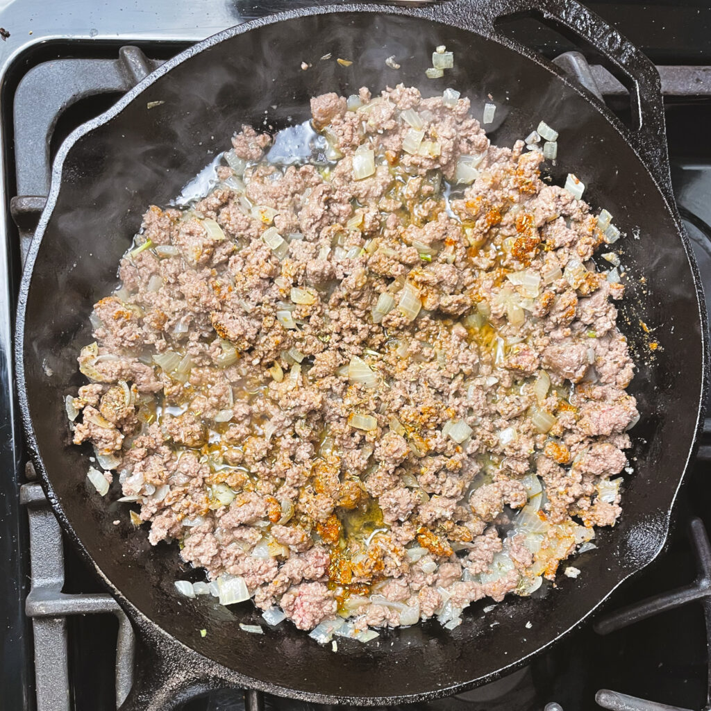 Sautéed onions and garlic with browned ground beef in a cast iron pan topped with seasonings