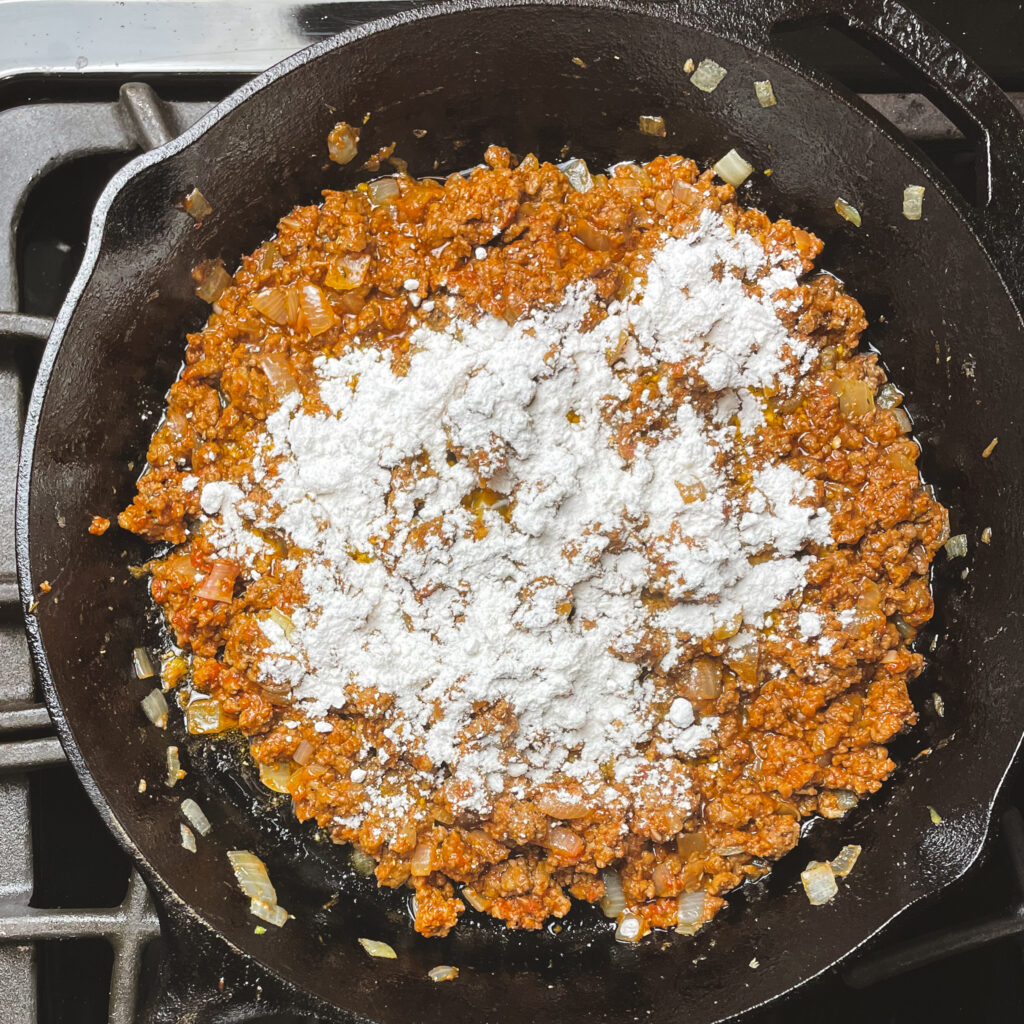 Ground beef mixture in a cast iron pan with flour sprinkled on top