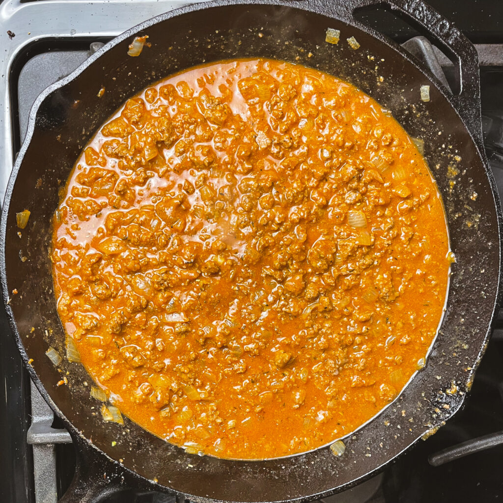 ground beef mixture in a cast iron pan with flour stirred in, and broth mixed in to create a gravy.