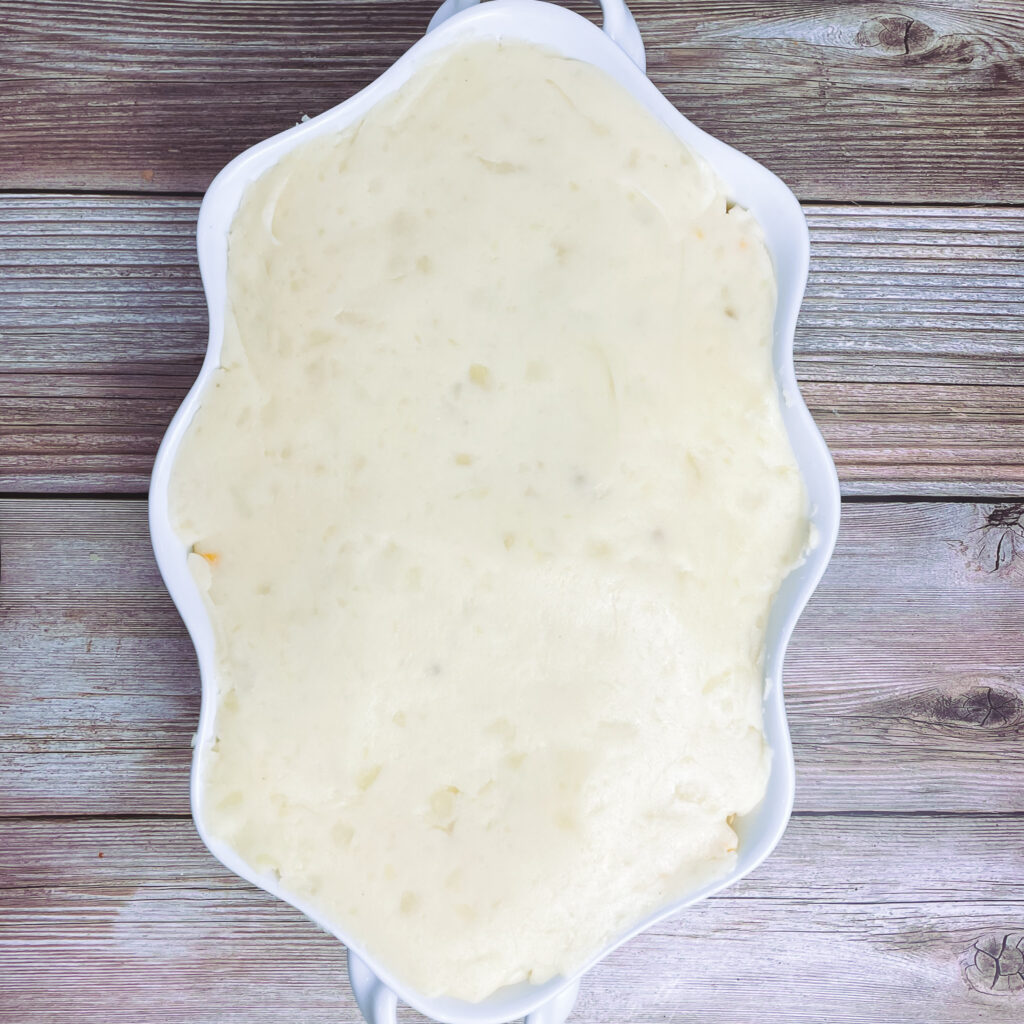 Mashed potatoes spread out evenly on top of the corn layer in a white casserole dish