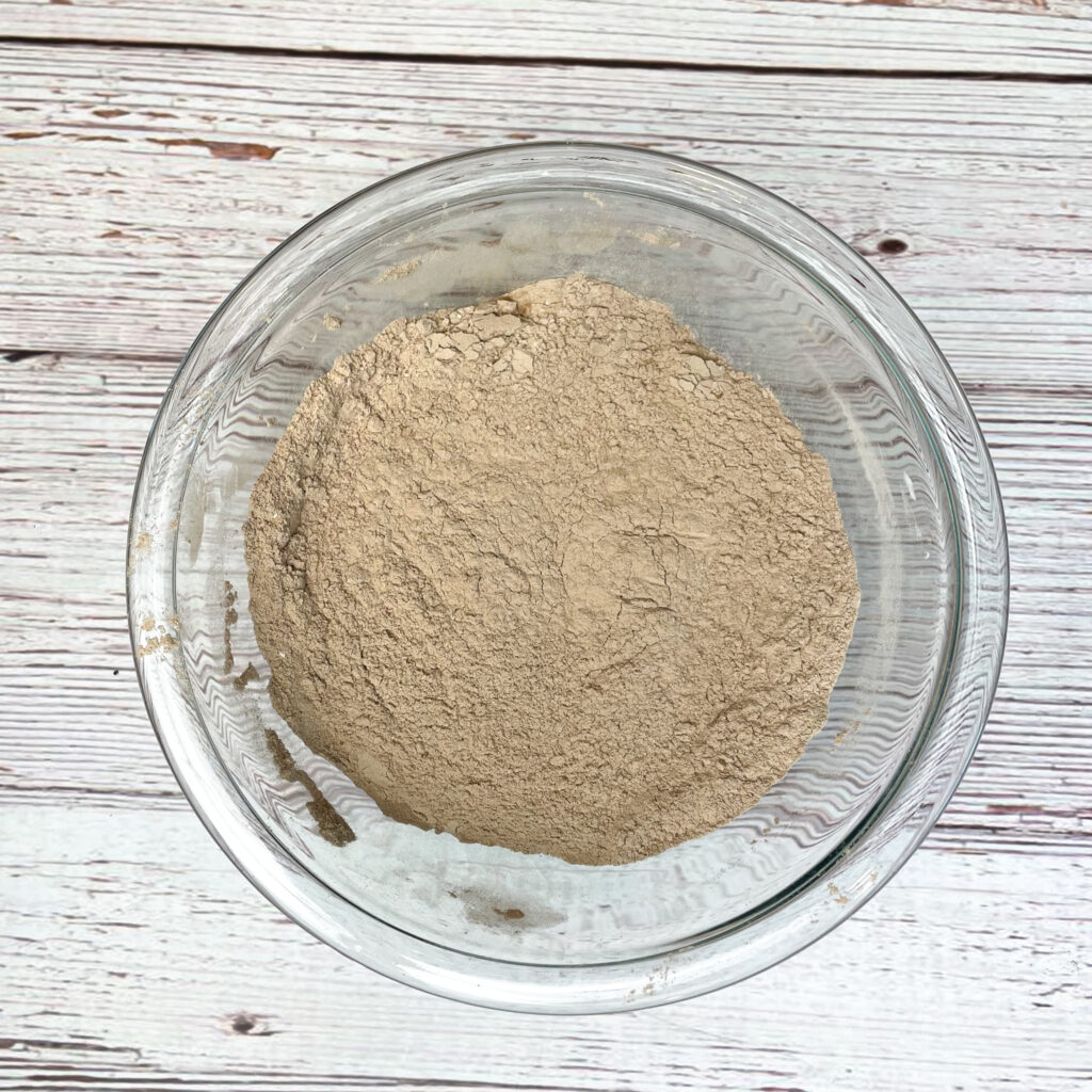 Dry ingredients for red velvet Crumbl cookies in a medium glass bowl, mixed together on a white wooden table.