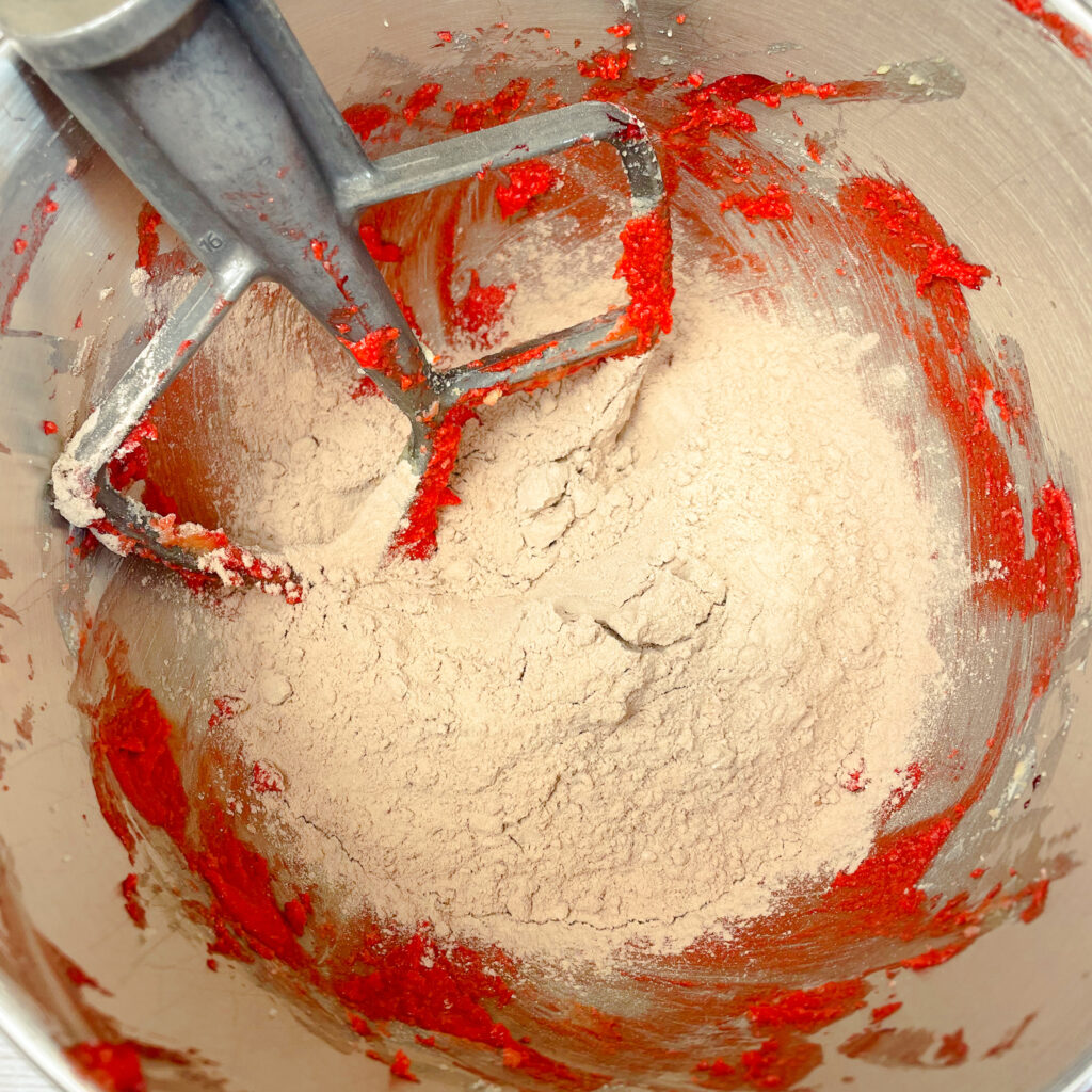 Wet ingredients for red velvet crumbl cookie dough creamed together in a mixing bowl, with the dry ingredients poured on top