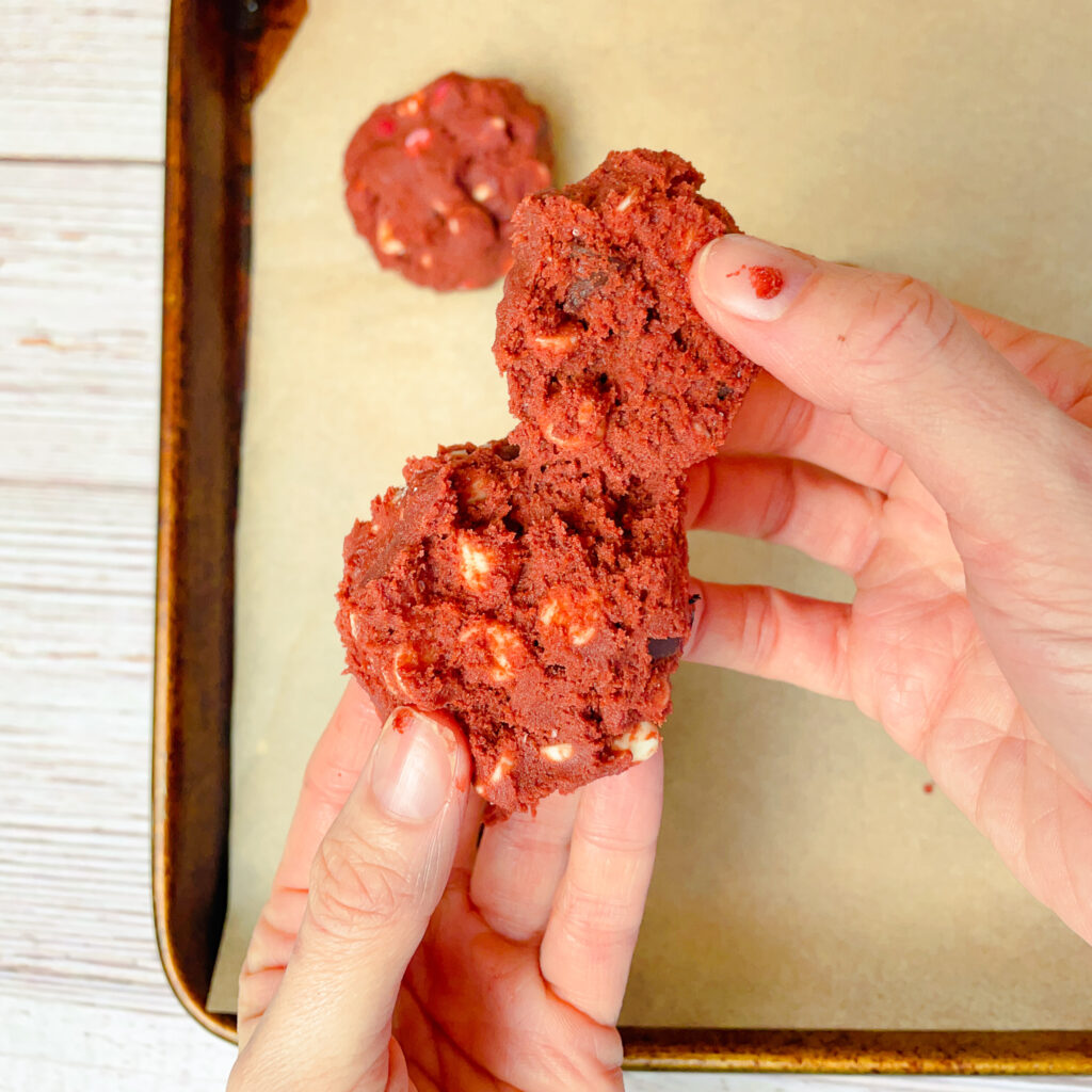 hands holding up a cookie dough ball split in half