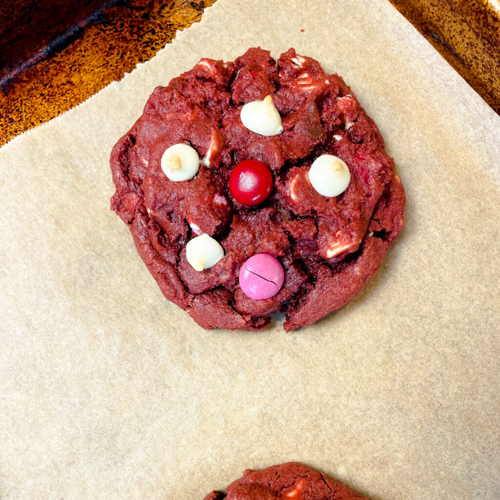 A red velvet Crumbl cookie on a baking sheet finished baking after pan banging.