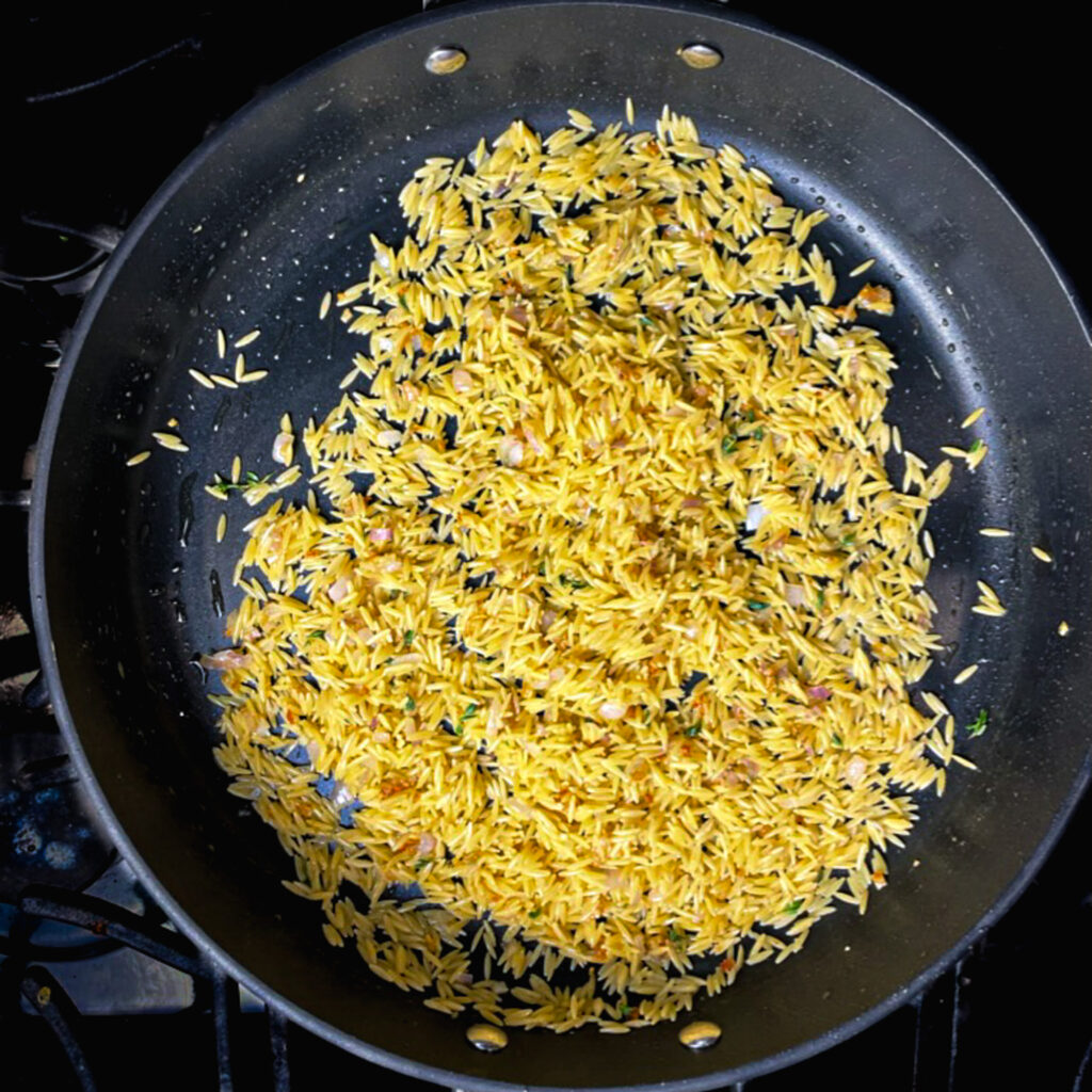 orzo cooking in a large fry pan.