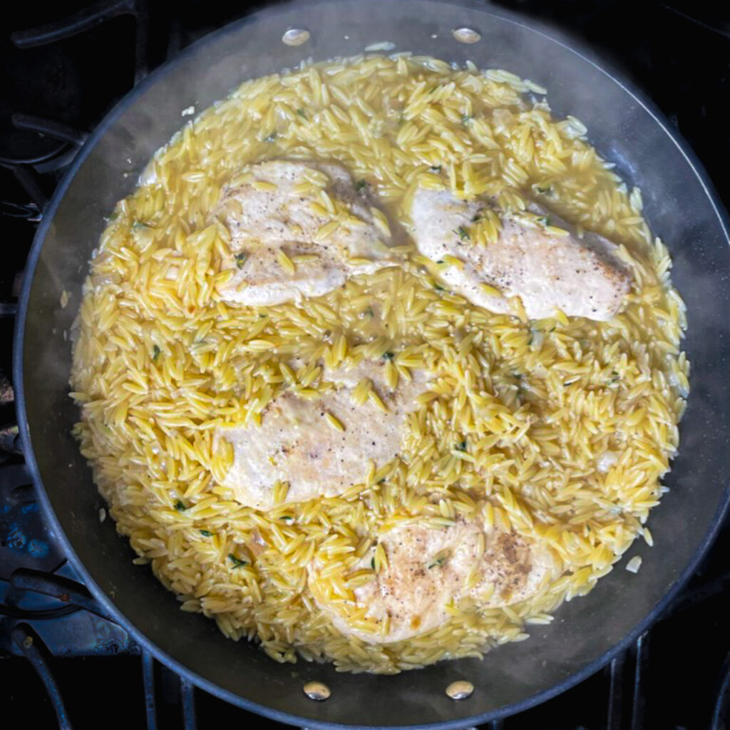 cooked orzo with cooked chicken breast in a large fry pan.
