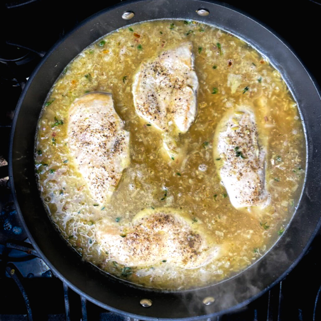 orzo, chicken broth, and whole cooked chicken breast in a large fry pan on the stove.