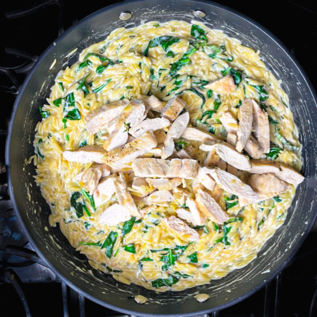 one pan lemon chicken orzo in a skillet on the stove with sliced chicken breast on top.