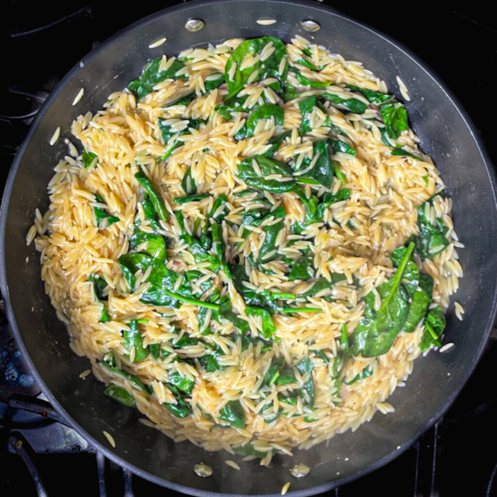 one pan lemon chicken orzo cooking with baby spinach stirred in.