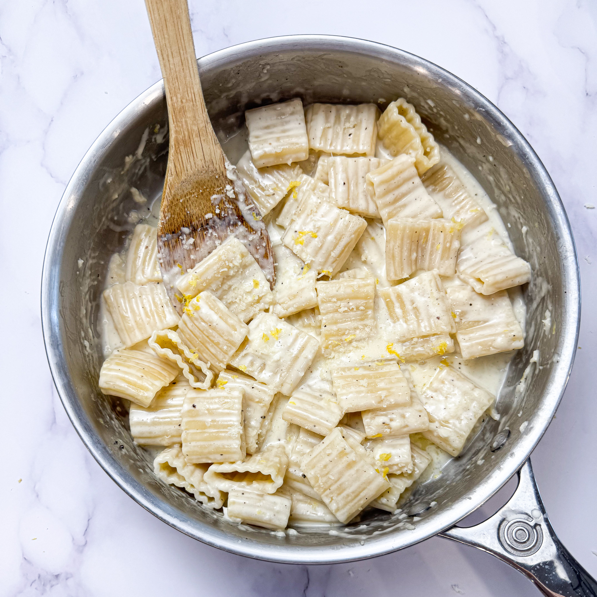 creamy lemon garlic pasta in a saute pan on the counter with a wooden serving spoon