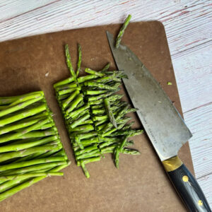 asparagus on a cutting board with the top 2 inches cut off next to a chef's knife.
