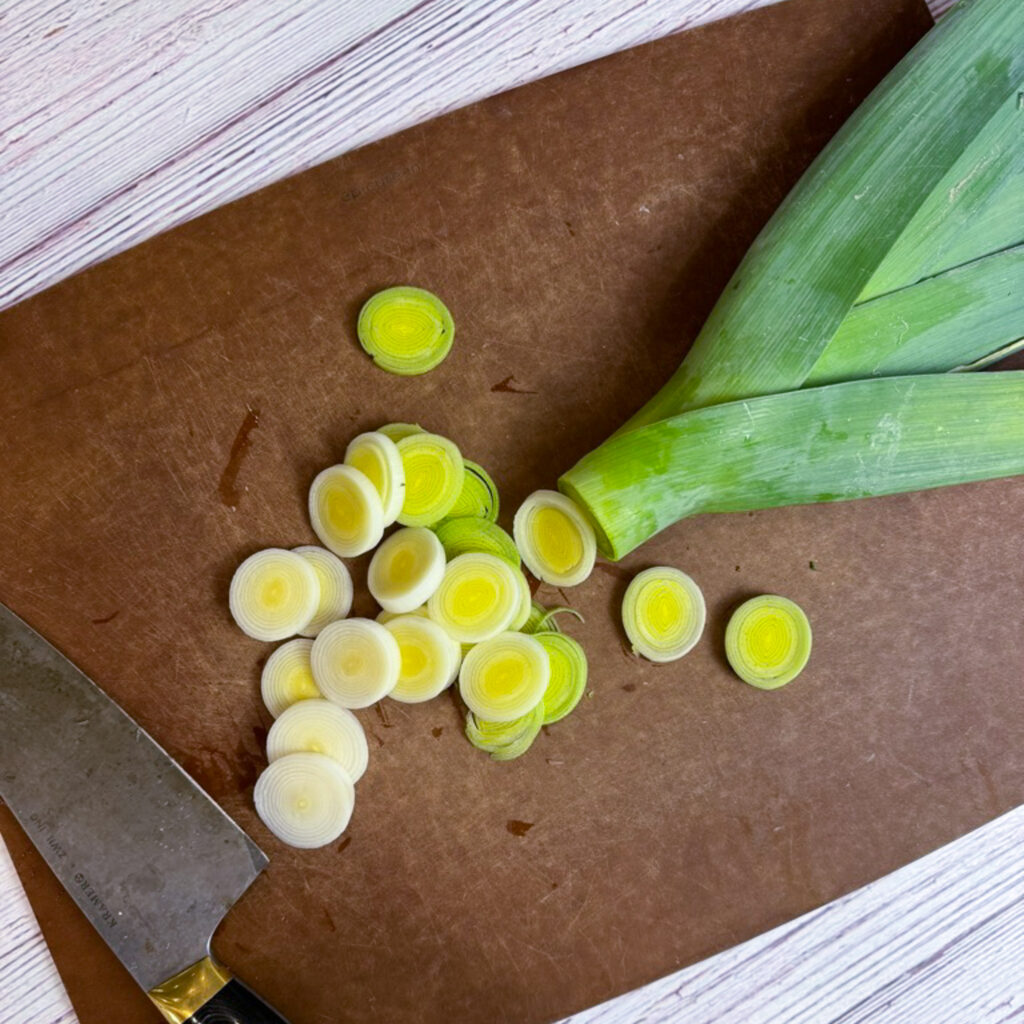 A leek on a cutting board sliced into 1/4 inch rounds up to the dark green top of the leek.