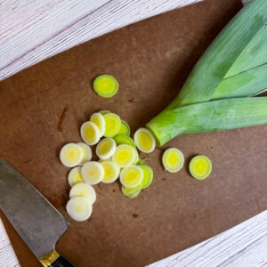 A leek on a cutting board sliced into 1/4 inch rounds up to the dark green top of the leek.