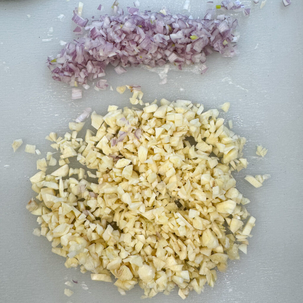 a close up image of chopped garlic and diced shallot on a cutting board