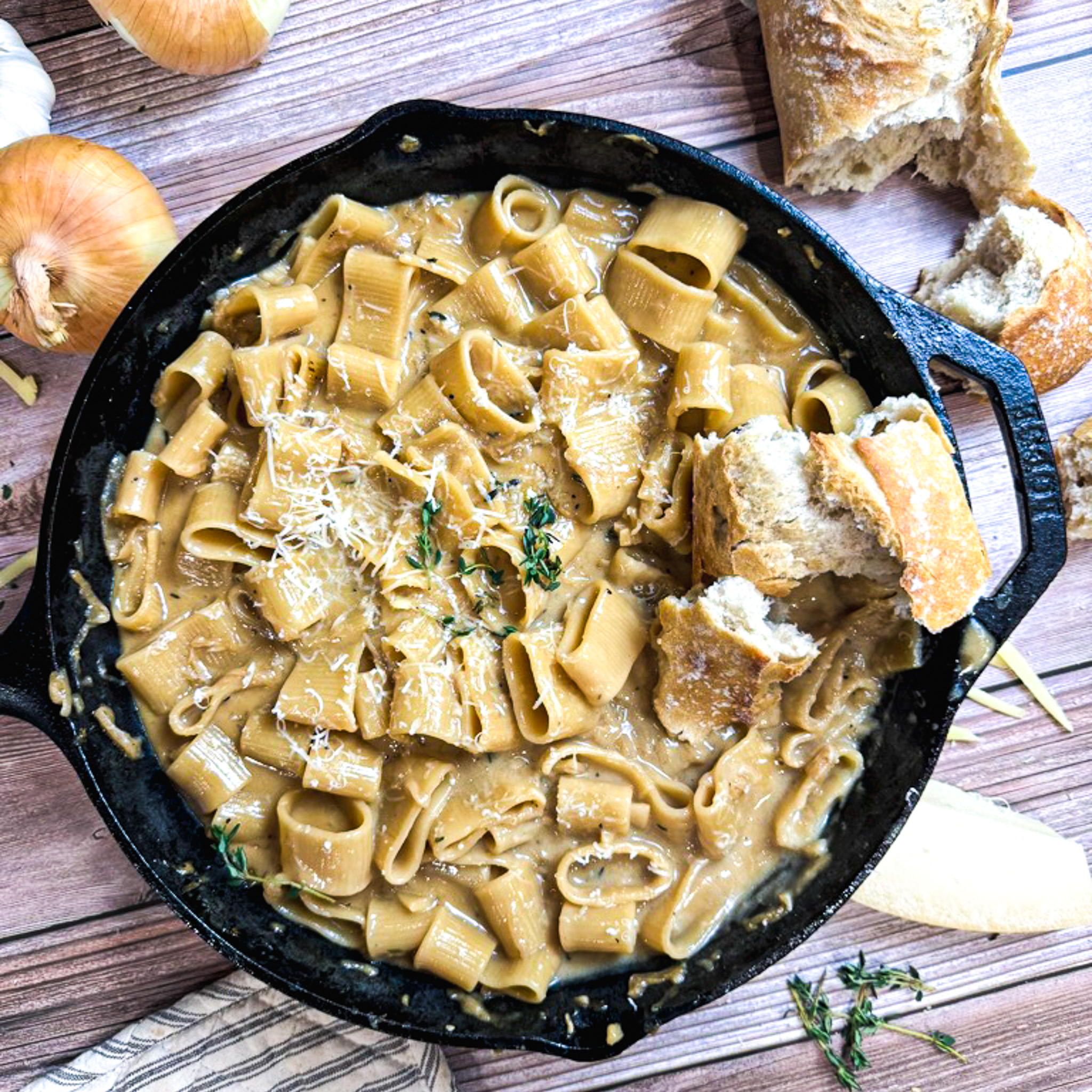one pot french onion pasta in a cast iron pan with crusty french bread dipping in it