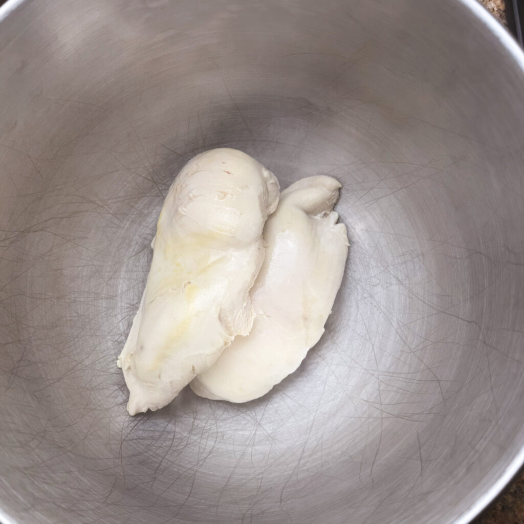 Cooked chicken breasts resting in a stainless steel mixing bowl, ready to be shredded for the soup.