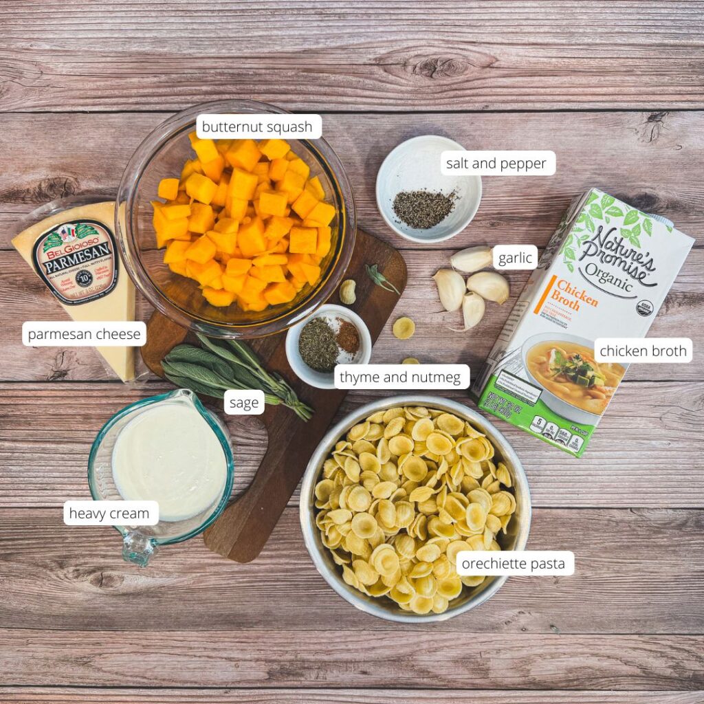 Ingredients for creamy butternut squash orecchiette pasta arranged on a rustic wooden table — cubed butternut squash, fresh sage, parmesan wedge, garlic cloves, chicken broth, heavy cream, spices, and a bowl of orecchiette pasta, all ready to make a cozy fall dinner.