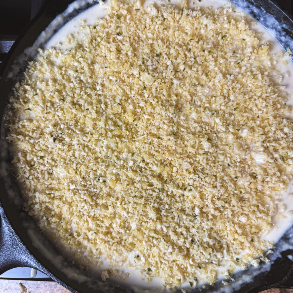 Creamy mac and cheese in a cast iron skillet topped with buttery panko-Parmesan crumbs, ready to bake until golden and bubbly.