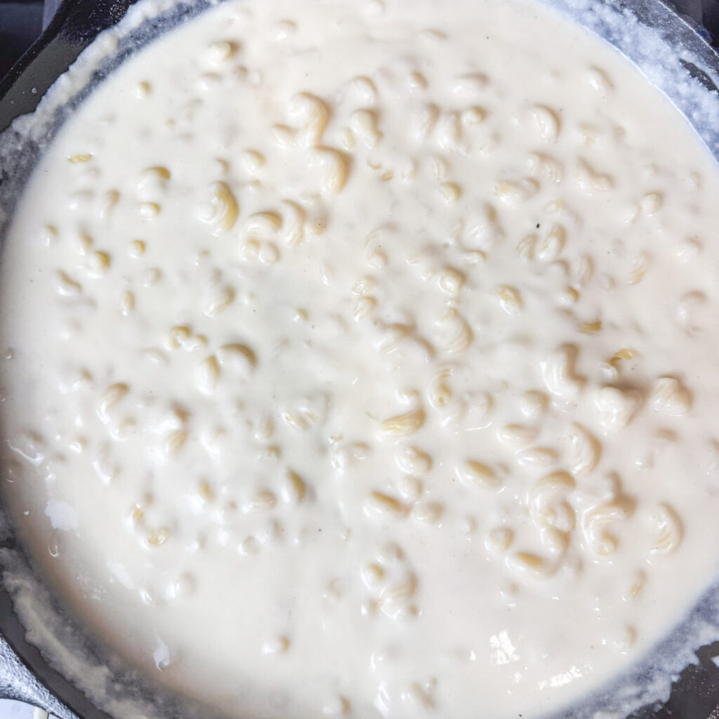Creamy cheese sauce simmering in a cast iron skillet with pasta stirred in. The sauce is rich and velvety, coating every piece for the ultimate homemade mac and cheese.