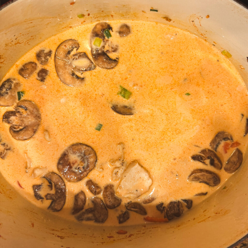 Simmering curry broth with sliced mushrooms and chicken, creating a rich, fragrant sauce for the noodles.