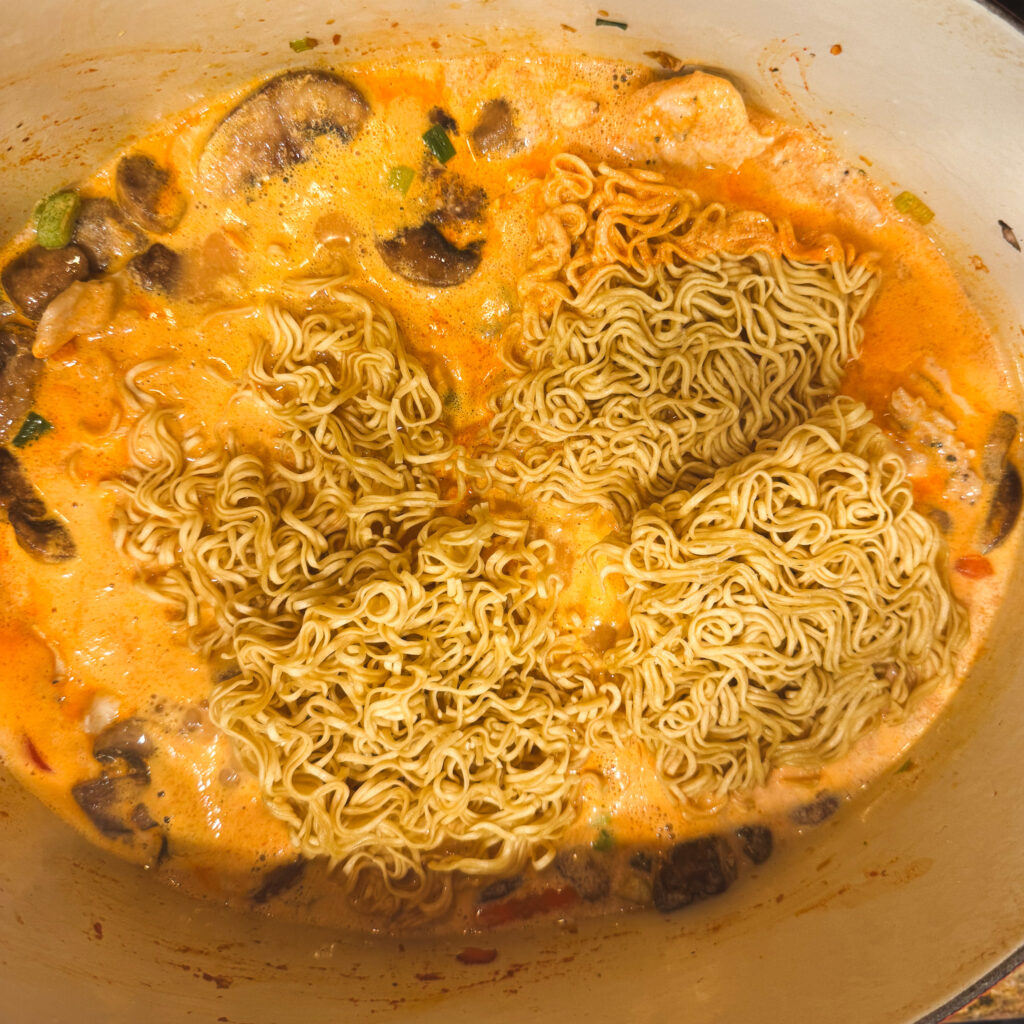 Uncooked ramen noodles nestled into the bubbling curry broth, just beginning to soften and soak up the flavor.