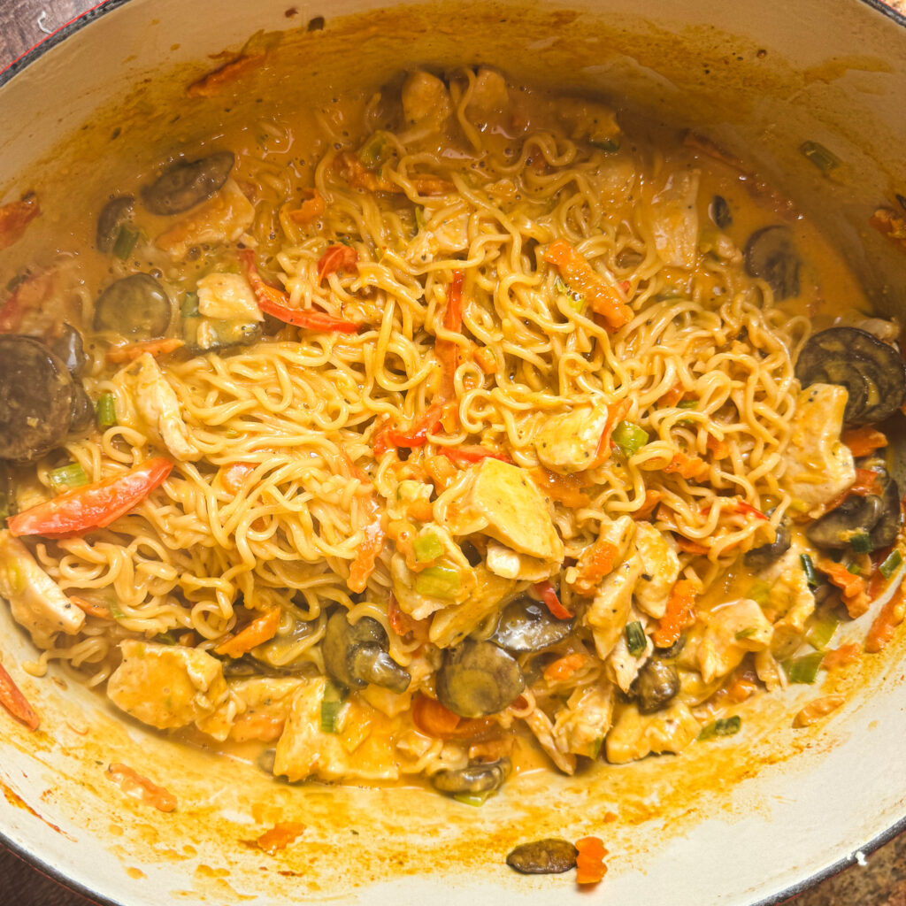 Dutch oven filled with creamy curry ramen noodles, tender chicken, peppers, carrots, and mushrooms all simmered together in one pot.